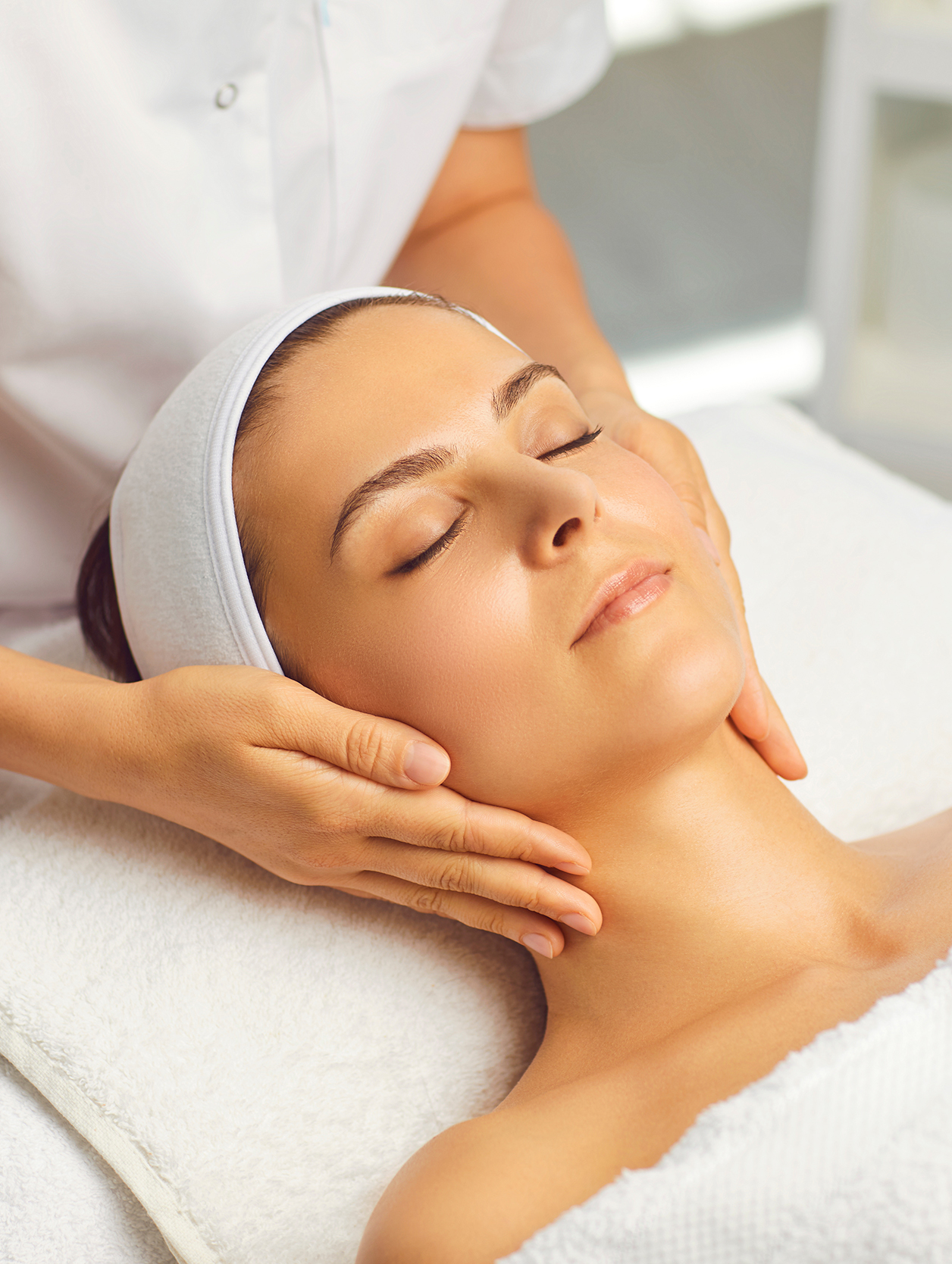 Hands of cosmetologist making manual relaxing rejuvenating facial massage for young woman